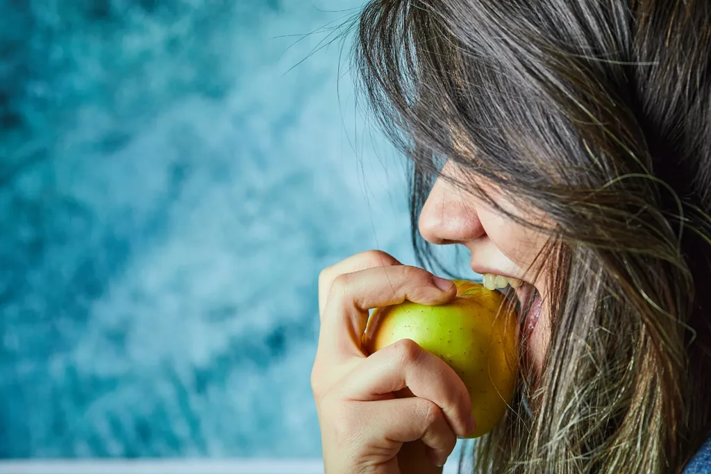 Woman eating an apple as part of a healthy diet to promote teeth health, emphasized by Montana Center for Implants and Dentures.