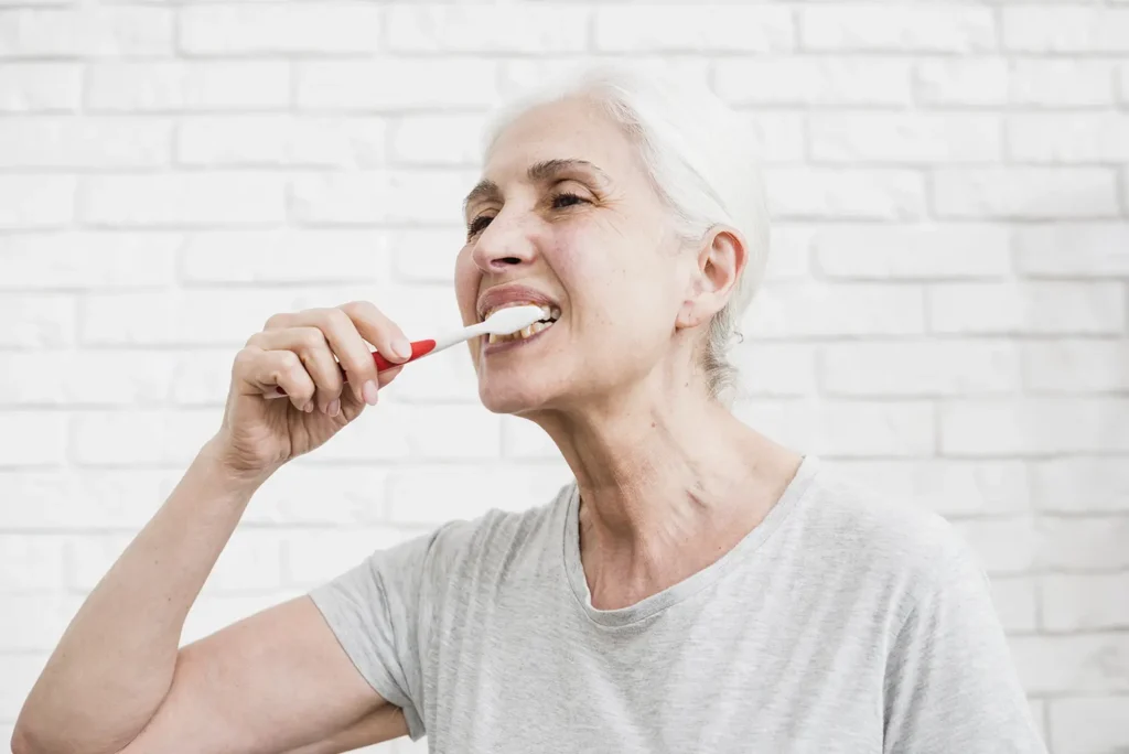 Senior woman practicing good oral health by brushing her teeth, recommended by Montana Center for Implants and Dentures.