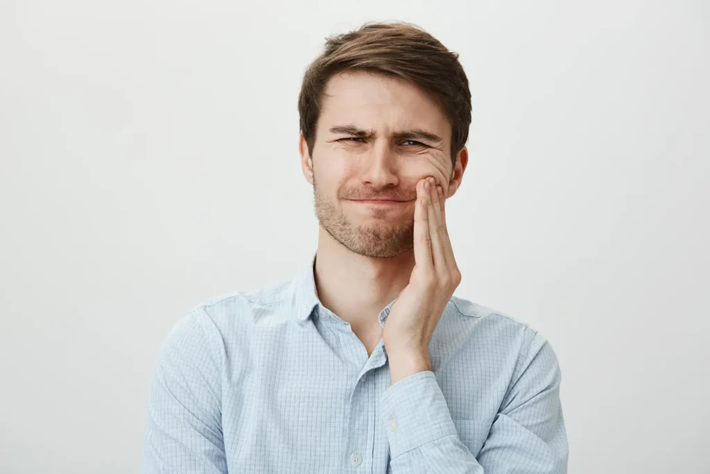 Man touching his cheek and grimacing from toothache, illustrating the pain and discomfort associated with tooth loss, and the benefits of dental implants from Montana Center for Implants and Dentures.