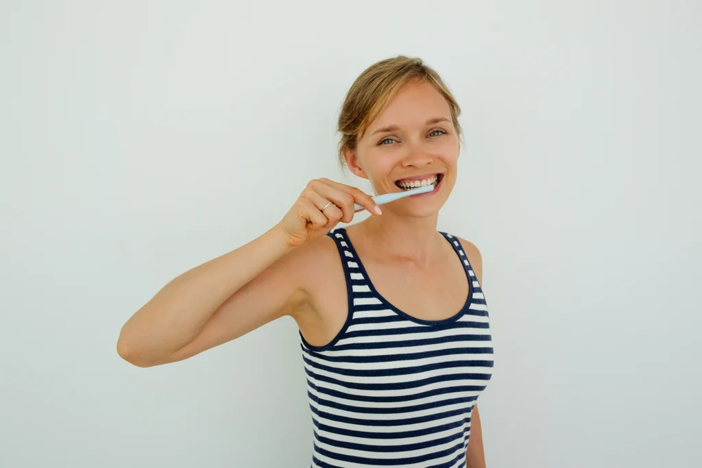 Cheerful woman brushing her teeth, demonstrating proper oral hygiene for cleaning All-on-4 implants, Montana Center for Implants and Dentures.